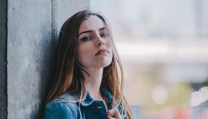Brunette woman wearing a denim jacket leans against a wall as she thinks about her dental anxiety