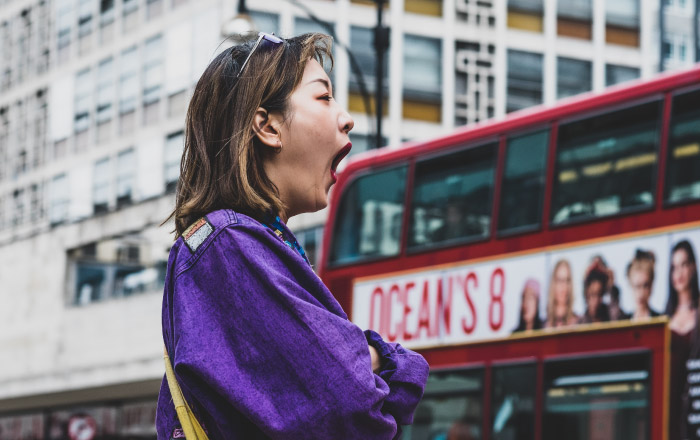 Brunette woman wearing a purple jacket yawns due to daytime sleepiness from sleep apnea