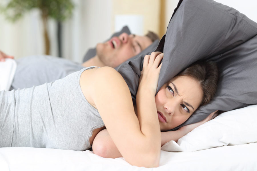 woman covers her head with a pillow to block out her partners snoring