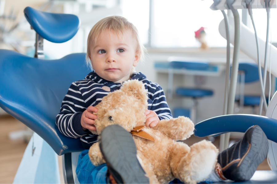 young boy holding a teddy bear sits in the dentist chair 