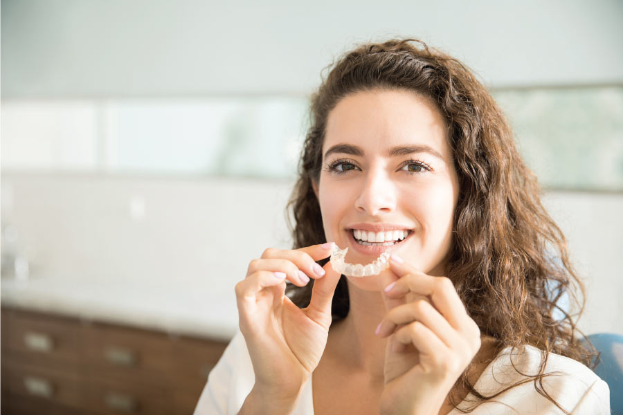 woman smiles as she prepares to insert her clear aligner to straighten teeth